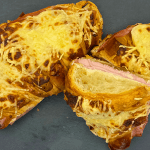 Croissants au jambon et fromage gratinés. Deux croissants dorés, garnis de jambon et de fromage fondant, présentés sur une ardoise noire. Parfait pour un dîner rapide et savoureux. Recette facile à réaliser à la maison.